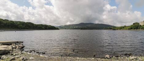 A rocky shoreline with a calm body of water, distant hills, and a partly cloudy sky.