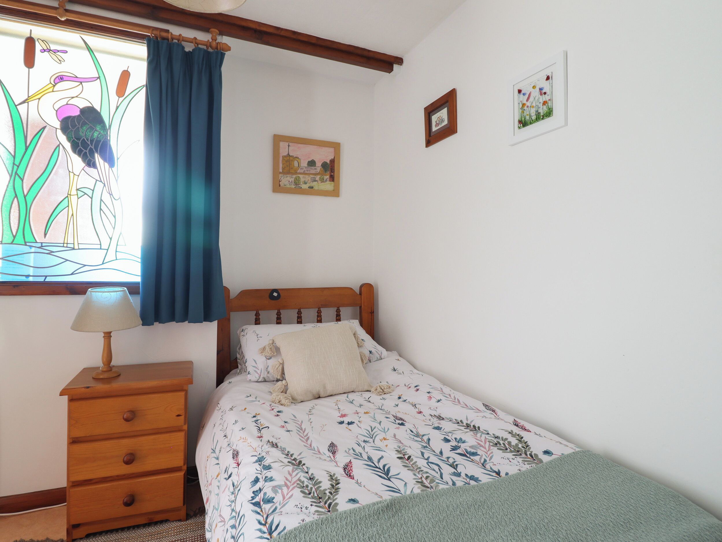 A bedroom with a wooden bed, a nightstand, a lamp, and a window with a stained glass view.