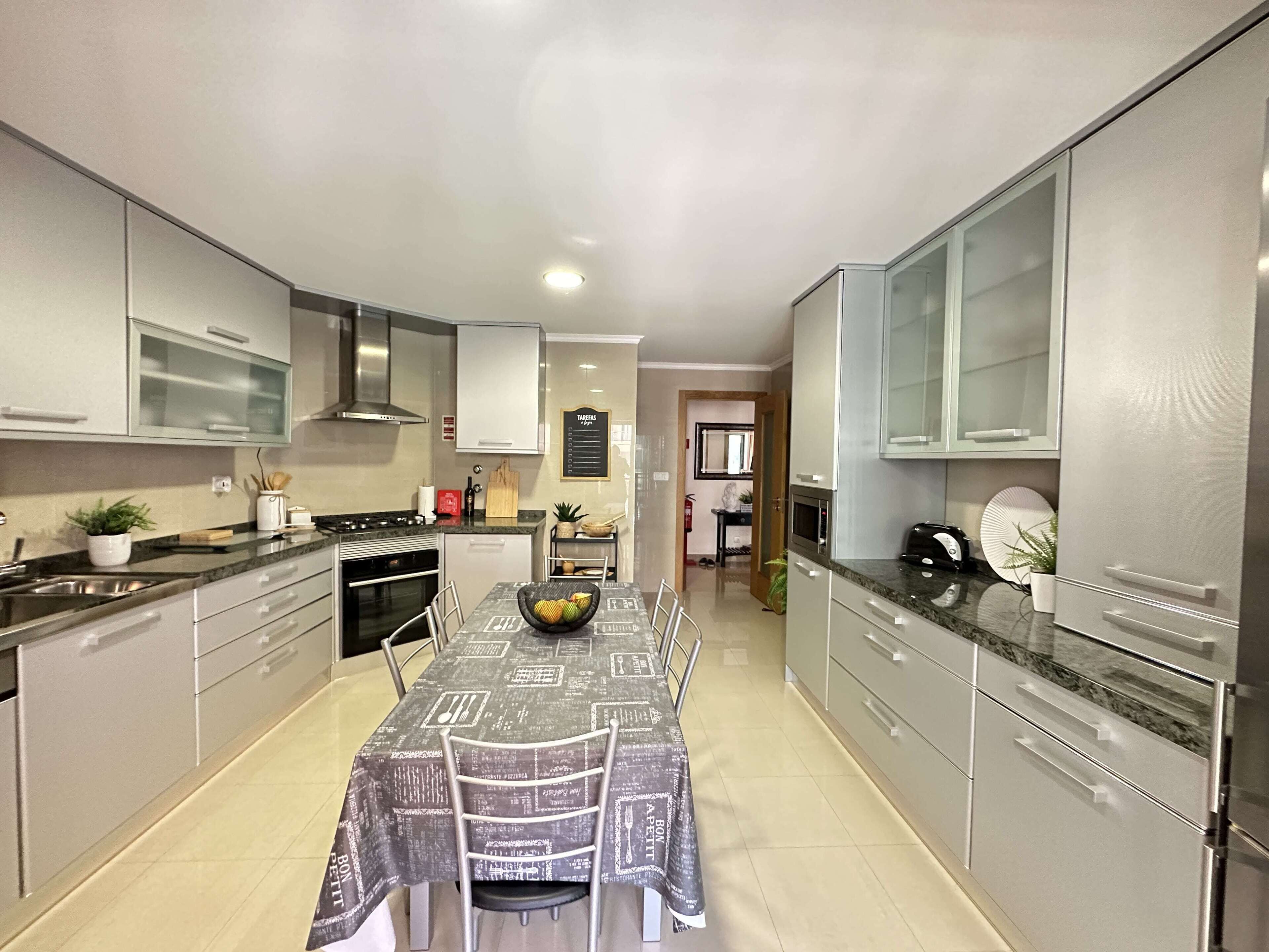 A modern kitchen with a central island, stainless steel appliances, and a dining area with a patterned tablecloth.