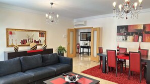 A modern living room with a black sofa, a red and black coffee table, and a chandelier. There is a dining area with red chairs and a red rug. - Ameijeira Lagos Apartment (Lagos)