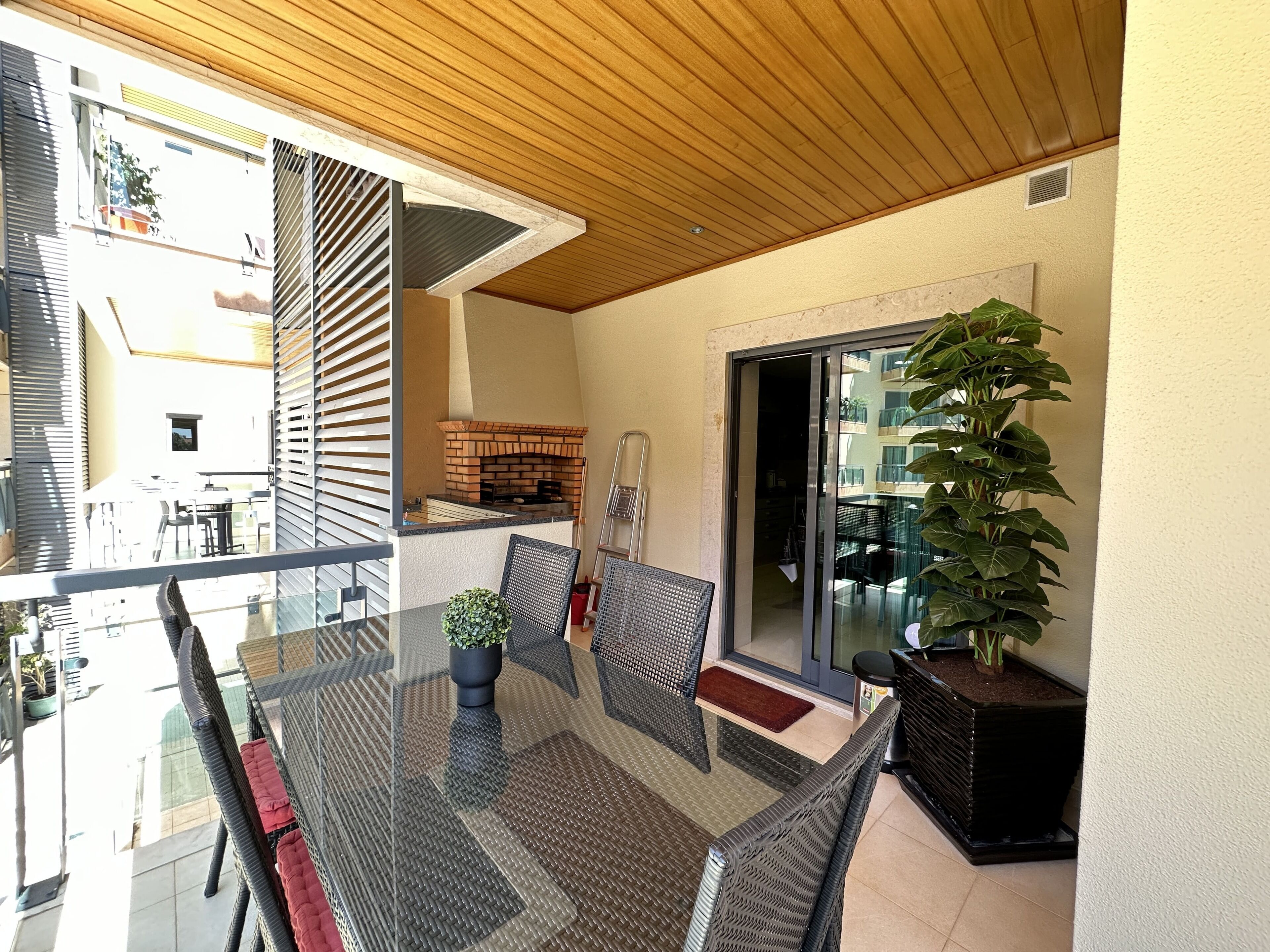 A balcony with a glass table, wicker chairs, and a potted plant.