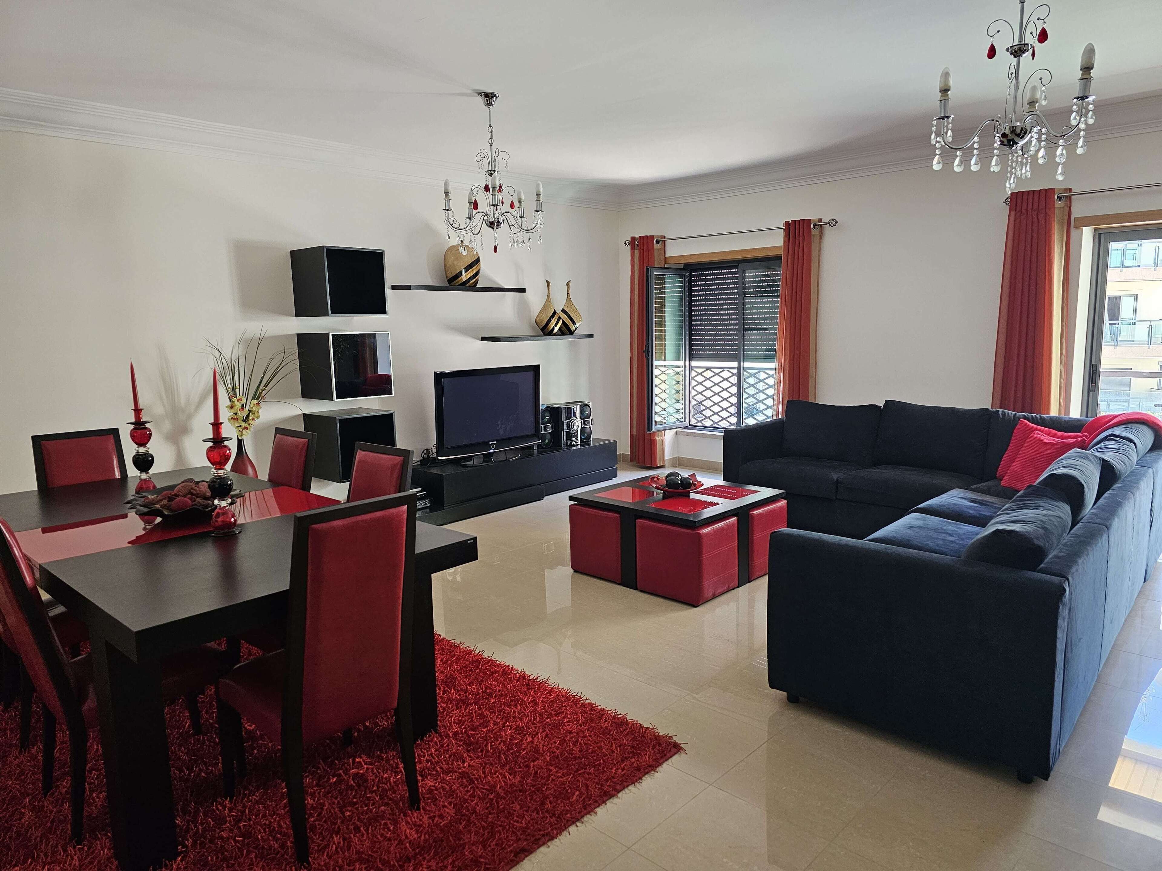 Uma sala de estar moderna com um sofá preto, cadeiras vermelhas, uma mesa de jantar e um candelabro.