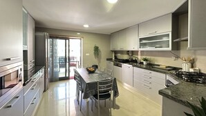 A modern kitchen with stainless steel appliances, a dining area with a table and chairs, and a sliding glass door leading to a balcony. - Ameijeira Lagos Apartment (Lagos)
