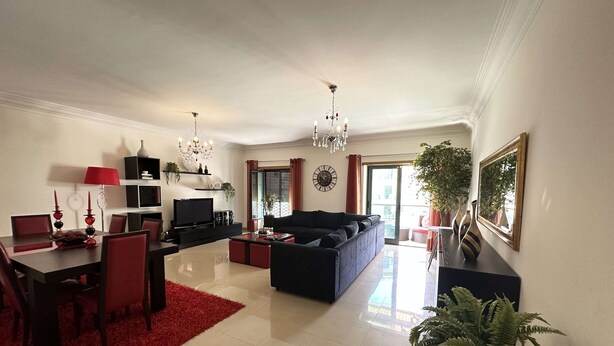 A spacious living room with a black sofa, red chairs, a dining table, and a TV. There is a chandelier, a red rug, and a potted plant. - Ameijeira Lagos Apartment (Lagos)
