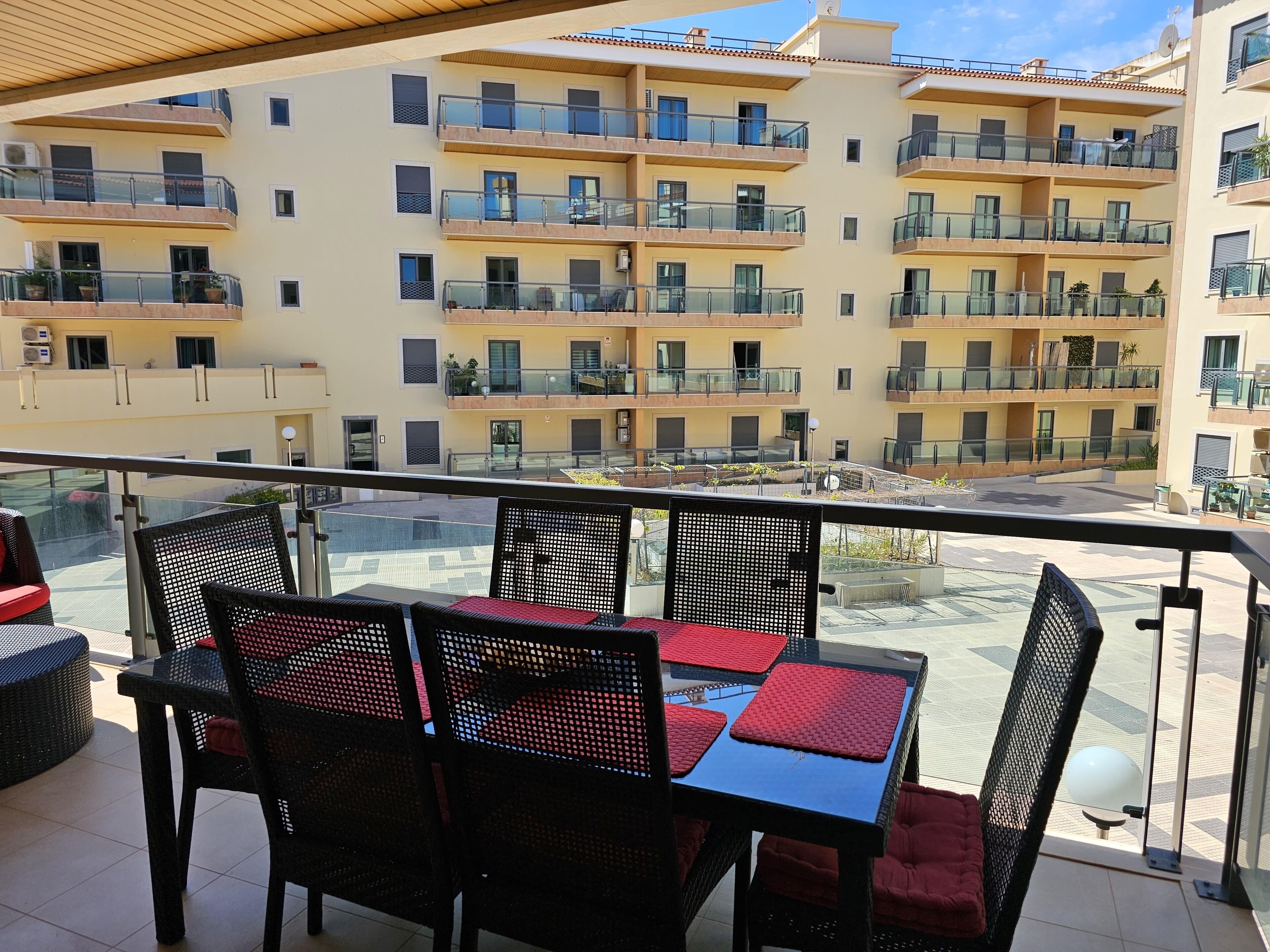 Un balcon aménagé avec du mobilier d’extérieur, une vue sur un immeuble à plusieurs étages doté de balcons, et un sol carrelé.