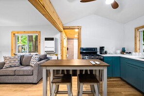 Une cuisine moderne équipée d’une cuisinière à gaz, d’une table à manger avec deux chaises, d’un canapé et d’une fenêtre donnant sur les arbres.