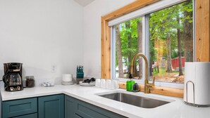 A modern kitchen with a large window, a coffee maker, and a sink. - Cozy l Hot Tub+Sauna l Arbutus Lake l Close to TC (Traverse City)