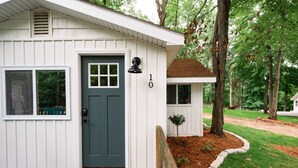 A small, single-story house with a dark green front door, white siding, and a mailbox. - Cozy l Hot Tub+Sauna l Arbutus Lake l Close to TC (Traverse City)