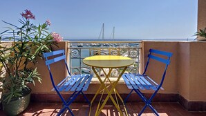 A balcony with a yellow table and blue chairs, overlooking a marina with boats. - (102) Le superbe au Palais (Vallauris)