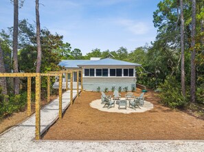 A house with a blue roof, surrounded by a wooden deck and a small patio area with four chairs.