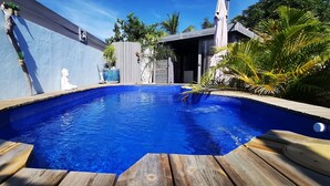 Une piscine dotée d’une terrasse en bois, entourée d’un mur bleu et d’une clôture en bois.