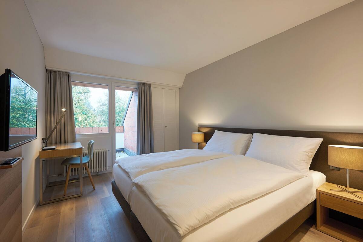 Hotelkamer met een groot bed, een bureau, een stoel, een televisie en een raam met gordijnen.