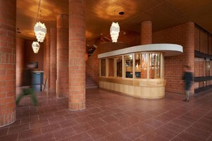Un vestíbulo amplio con columnas de ladrillo, un mostrador de recepción curvo y candelabros colgantes.