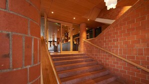 A staircase with wooden handrails and red brick walls, leading to a glass door entrance. - Parkhotel Wallberg (Volketswil)