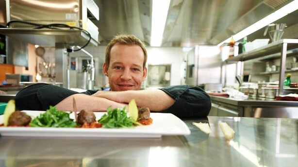 A person seated at a table with a white plate of food in a modern kitchen setting. - Parkhotel Wallberg (Volketswil)