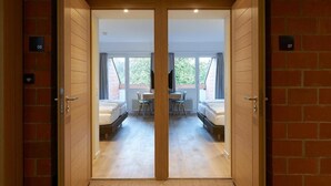 A hotel room with a wooden door, a bed, a small table, and a window. - Parkhotel Wallberg (Volketswil)