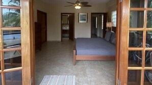 A room with a bed, a ceiling fan, and a view through a glass door. - Magnificent Belize Townhouse-Pool-Private Island (Placencia)