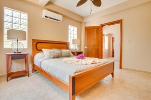 A bedroom with a wooden bed, two bedside tables with lamps, a large window, and an air conditioning unit. - Magnificent Belize Townhouse-Pool-Private Island (Placencia)
