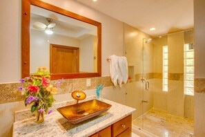 A bathroom with a marble countertop, a vessel sink, a mirror, a ceiling fan, and a glass-enclosed shower. - Magnificent Belize Townhouse-Pool-Private Island (Placencia)