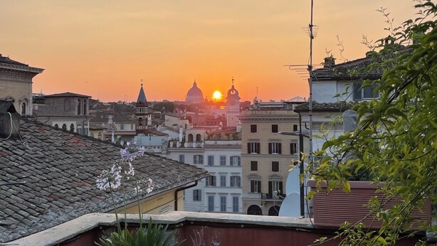 A terrace with a table and chairs, overlooking a cityscape at sunset.