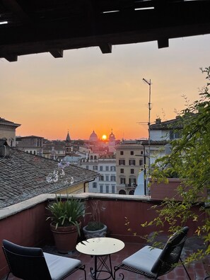 A terrace with a table and chairs, overlooking a cityscape at sunset. - Breathtaking Terrace and Penthouse in the Center of Rome (Roma)