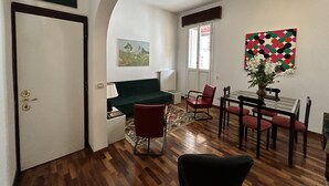 A living room with a sofa, chairs, a dining table, and a painting on the wall.