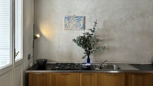A kitchen with a gas stove, a sink, wooden cabinets, a vase with greenery, and a painting on the wall.