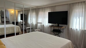 A hotel room with a large bed, a TV, a desk with a chair, and a mirror.