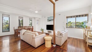 Un salon spacieux avec un plancher en bois, un grand canapé, une table basse ronde et un téléviseur.