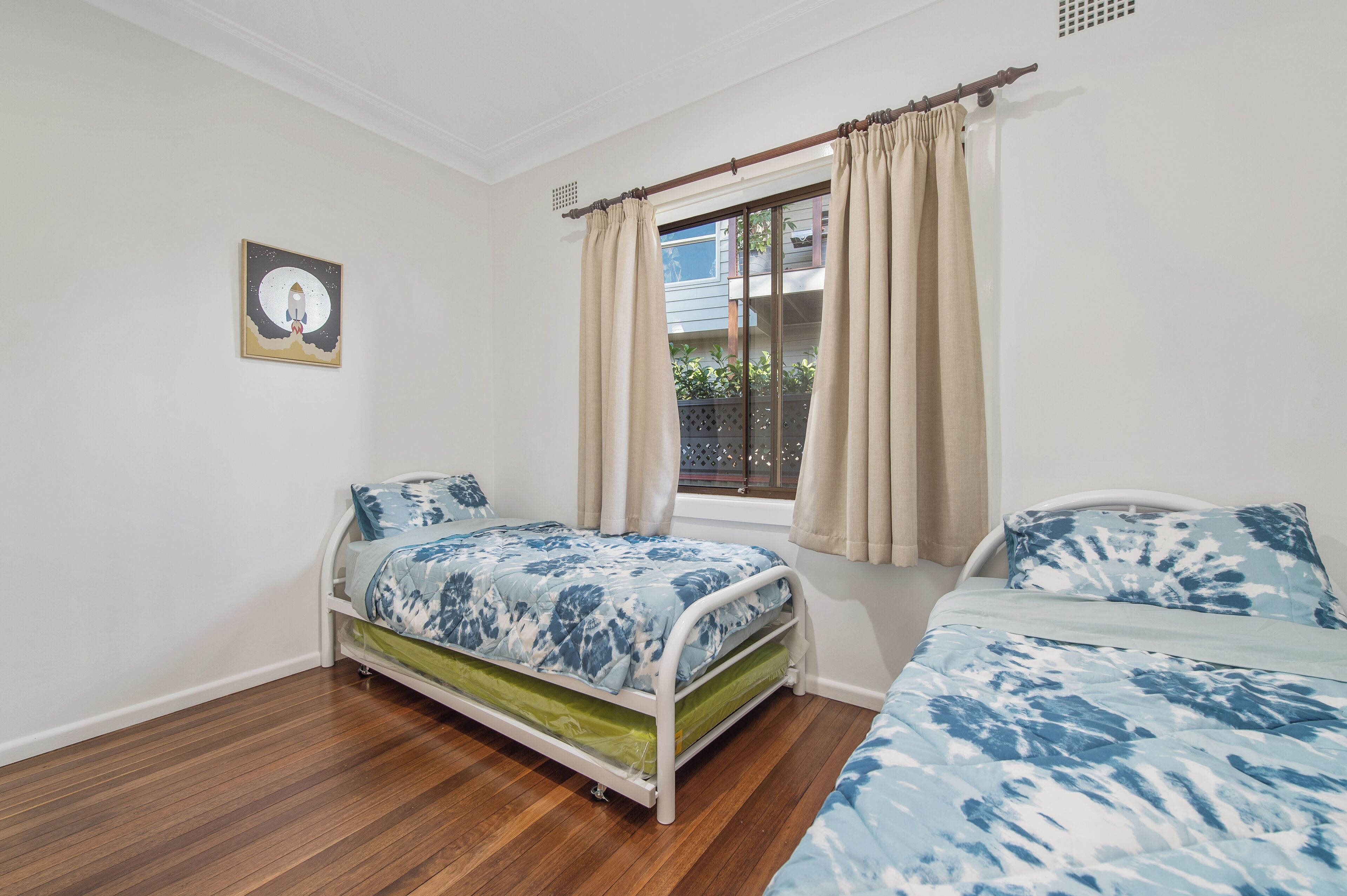 A bedroom with a bed, a window with curtains, a small balcony, and a wall-mounted picture.