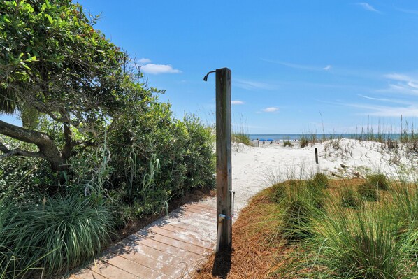 A wooden post with a metal structure attached, a wooden pathway, and a beach with sand dunes in the background.
