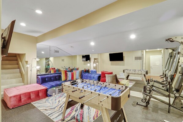 A room with a foosball table, a sofa, and a red ottoman.