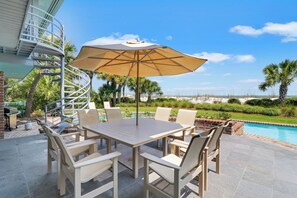 A poolside dining area with a table and chairs, an umbrella, and a view of the ocean. - Oceanfront home with huge windows and a panoramic views (Hilton Head)