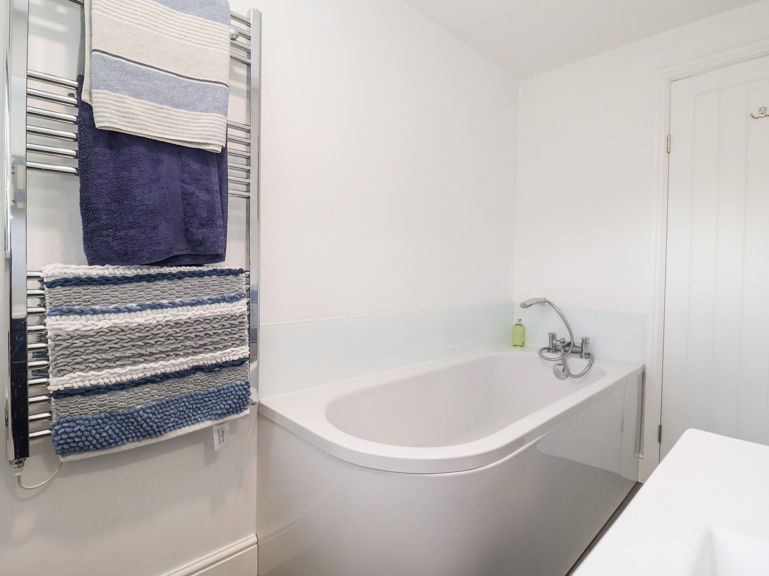 A bathroom with a white bathtub, a towel rack with multiple towels, and a small bottle of soap on the side.