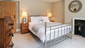 Een slaapkamer met een metalen bedframe, een houten kledingkast, nachtlampjes en een open haard.