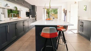 Een moderne keuken met donkergrijze kastjes, een wit aanrechtblad en twee barkrukken met gestreepte kussens.