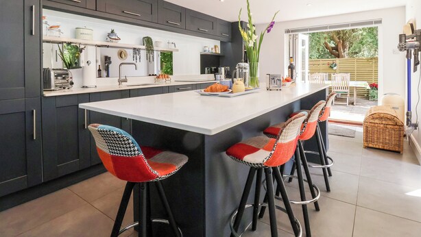 Een moderne keuken met donkere kastjes, een groot eiland en barstoelen.