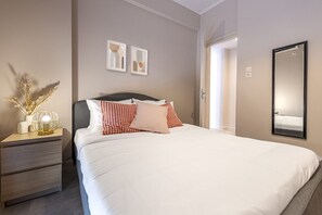 A neatly made bed with white and red checkered pillows, a bedside table with a lamp, and a mirror on the wall.