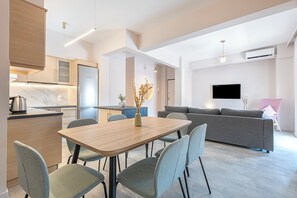 A modern kitchen with a dining area, a gray sofa, and a flat-screen TV.
