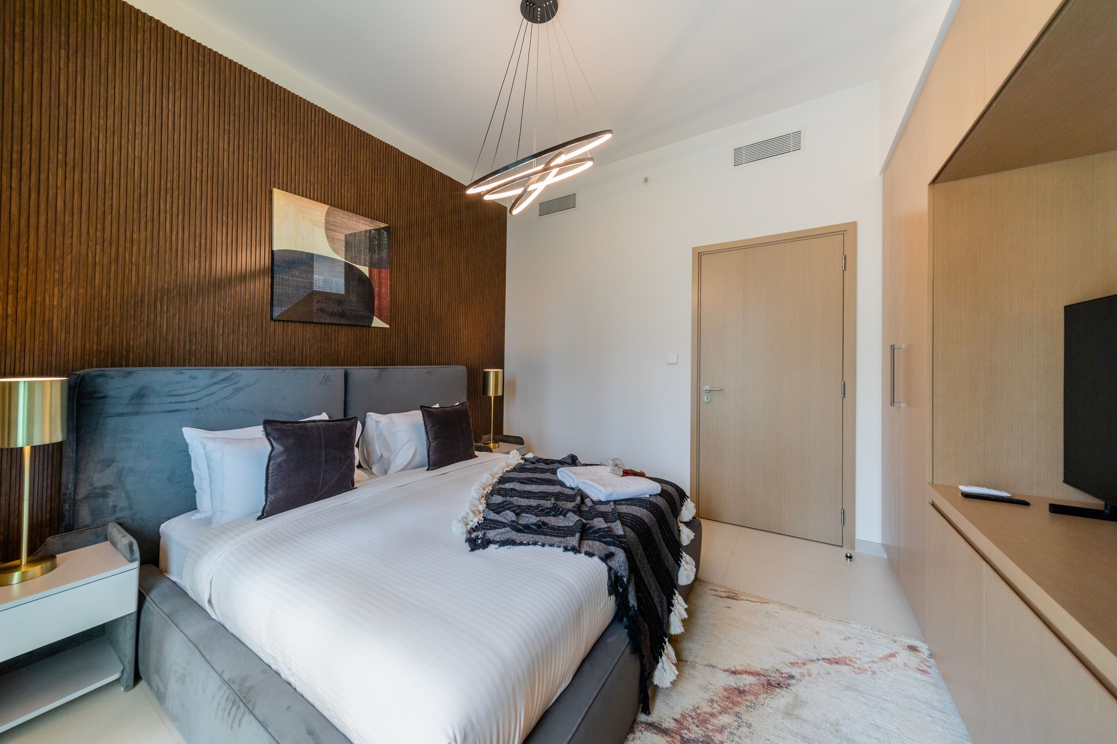 Ein modernes Schlafzimmer mit einem großen Bett, einer Holzwand und einem Flachbildfernseher.
