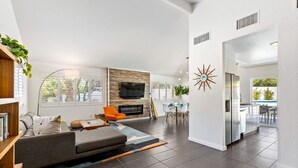 A modern living room with a fireplace, a sofa, and a dining area with a table and chairs. - Enchanting Escudero - Luxury PS Ranch Home! (Palm Springs)
