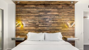 A modern bedroom with a wooden headboard, a large bed, two bedside tables, and two wall-mounted lights. - Enchanting Escudero - Luxury PS Ranch Home! (Palm Springs)