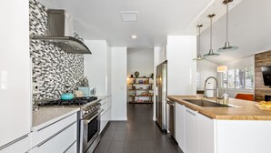 A modern kitchen with white cabinetry, a tiled backsplash, stainless steel appliances, and pendant lighting. - Enchanting Escudero - Luxury PS Ranch Home! (Palm Springs)