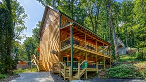A two-story log cabin with a balcony, surrounded by dense forest.
