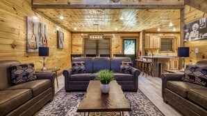 A cozy log cabin interior with a central seating area, a kitchen, and a dining area.