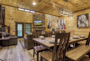A wooden interior with a dining area, sofas, and a television mounted on a stone wall.