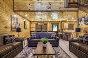 A cozy log cabin interior with a central seating area, a kitchen, and a dining space.