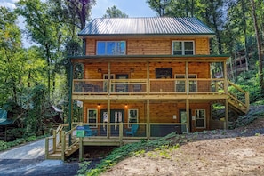 A two-story log cabin with a balcony, surrounded by forest.