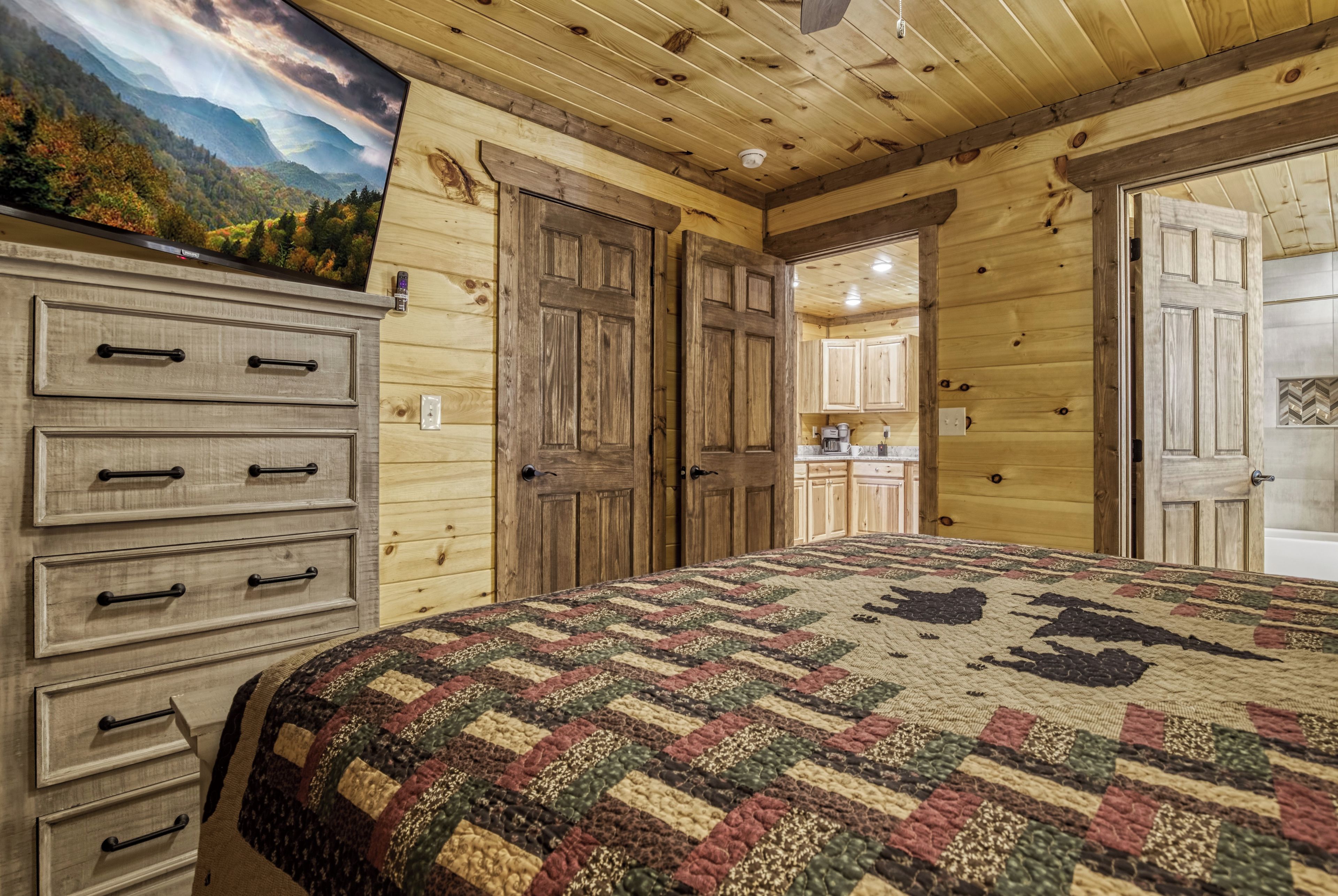 A wooden interior with a bed, dresser, and a view of a kitchen area.