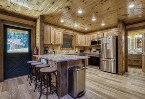 A modern kitchen with wooden cabinetry, a marble countertop, stainless steel appliances, and a bar stool area.